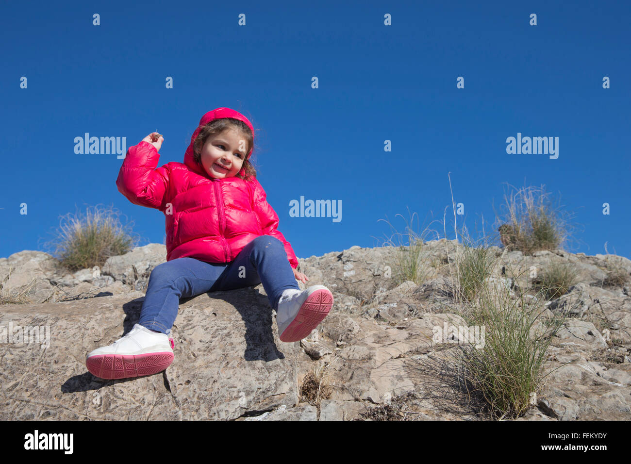 Schöne kleine Mädchen werfen Steinchen, Kamera auf Felsen sitzend Stockfoto