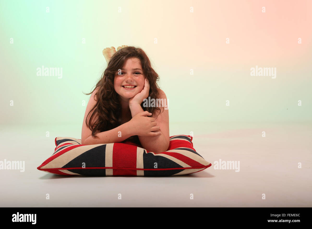 Eine schöne junge Brünette Mädchen umarmt ihr Kissen mit den Union Jack Farben drauf. Stockfoto