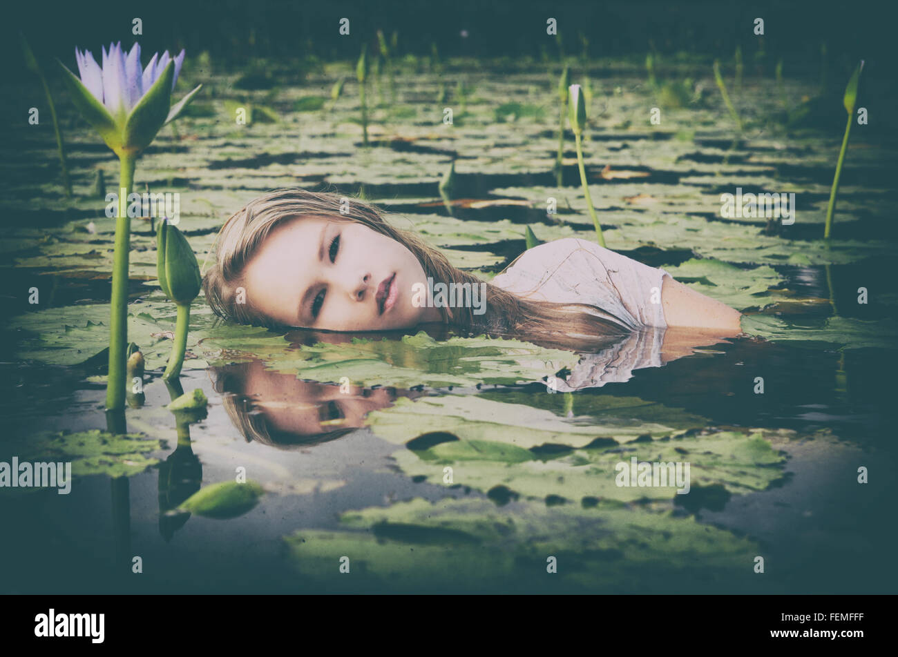 Eine schöne junge blonde Frau schwimmt unter den lila Lilien in einem Teich oder See in einem künstlerischen Ambiente. Gefilterte Bilder. Stockfoto