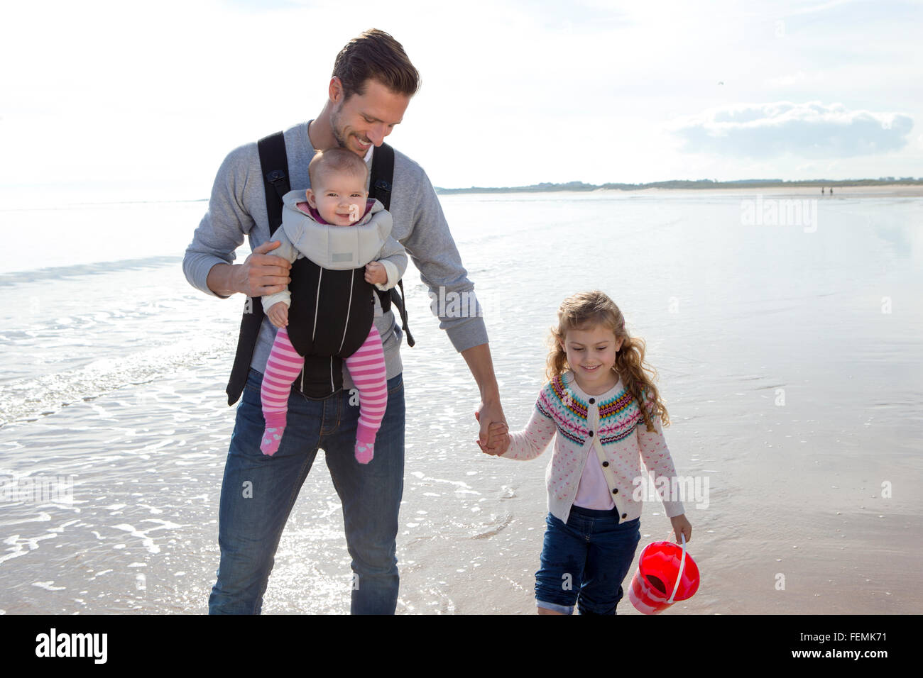 Junger Vater am Strand mit seinen beiden Töchtern. Stockfoto