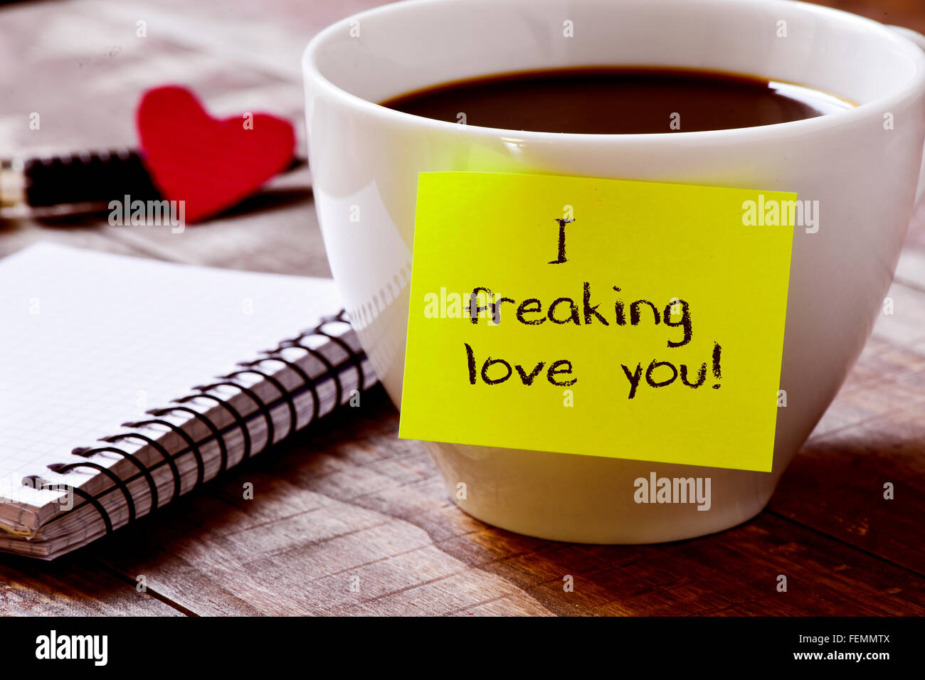 Nahaufnahme von einem gelben klebrigen Stelle mit dem Text ich freaking Liebe, die Sie neben einer Tasse Kaffee auf einem rustikalen Holztisch zugeordnet Stockfoto