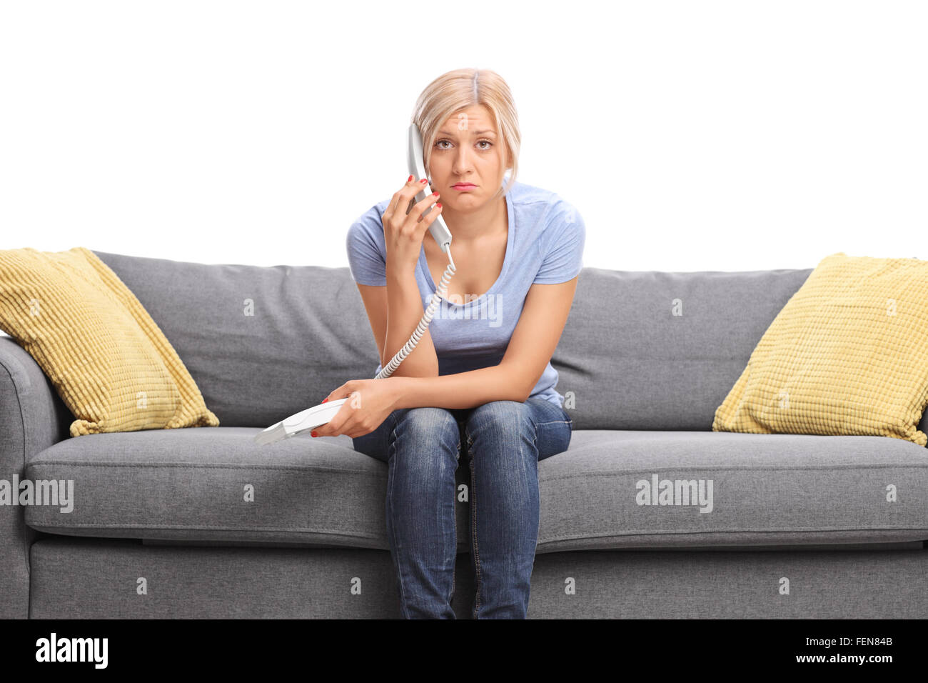 Trauriges Mädchen Gespräch am Telefon sitzt auf einem grauen Sofa und schaut in die Kamera, die isoliert auf weißem Hintergrund Stockfoto
