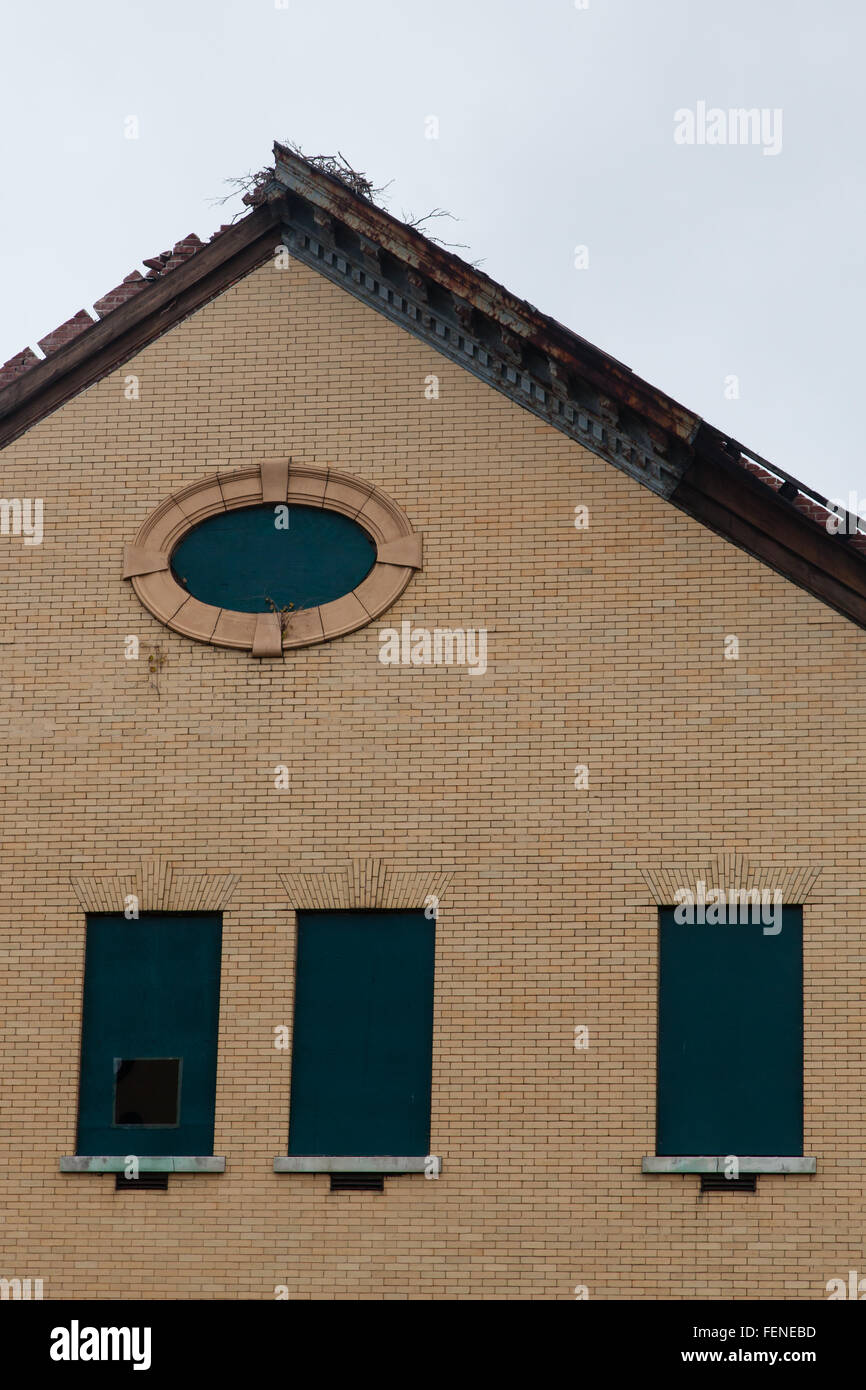 Die Traufe und Höhepunkt eines Dachs sind auf einem alten Backsteingebäude gesehen. Das Dach ist reparaturbedürftig. Stockfoto