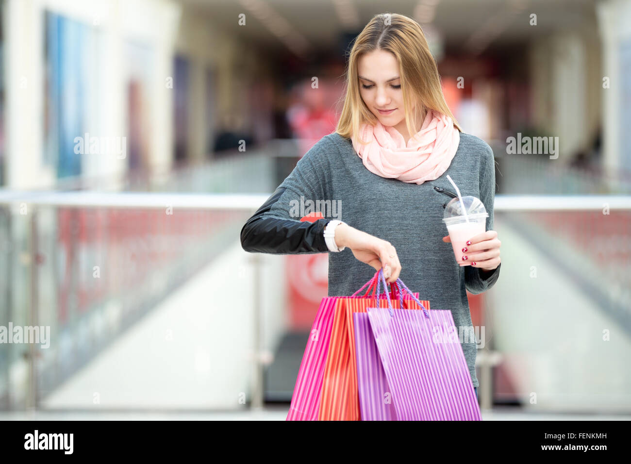 Junge Käufer Frau sah auf ihre Uhr während des Tragens Papiertüten mit Einkäufen und Milchshake Stockfoto