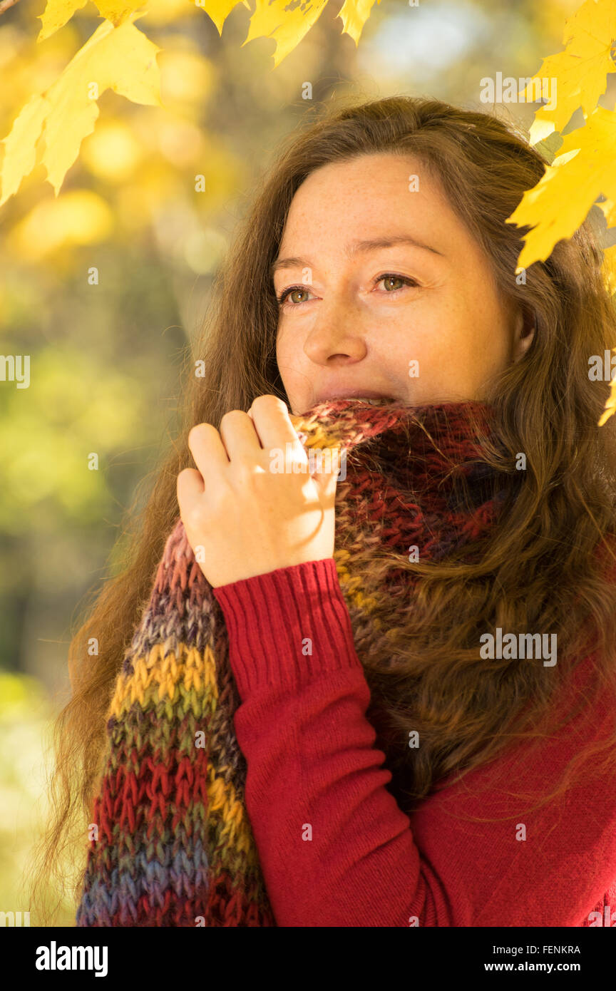 Frau mit braunen Haaren im herbstlichen Wald. Mit roten Pullover und Schal bunt gekleidet. Stockfoto