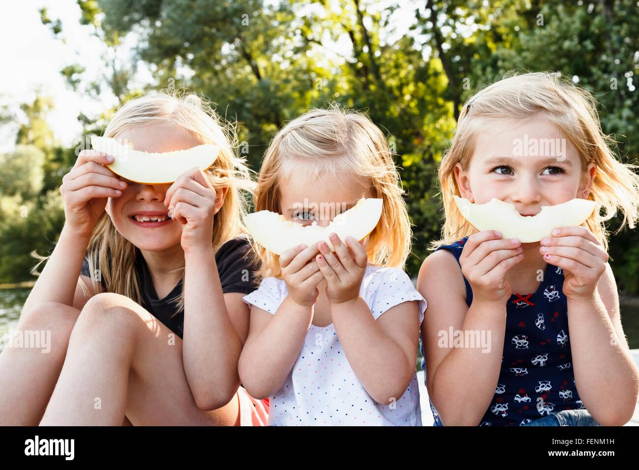 Porträt von drei jungen Schwestern hält lächelnd Melone vor Gesicht im park Stockfoto