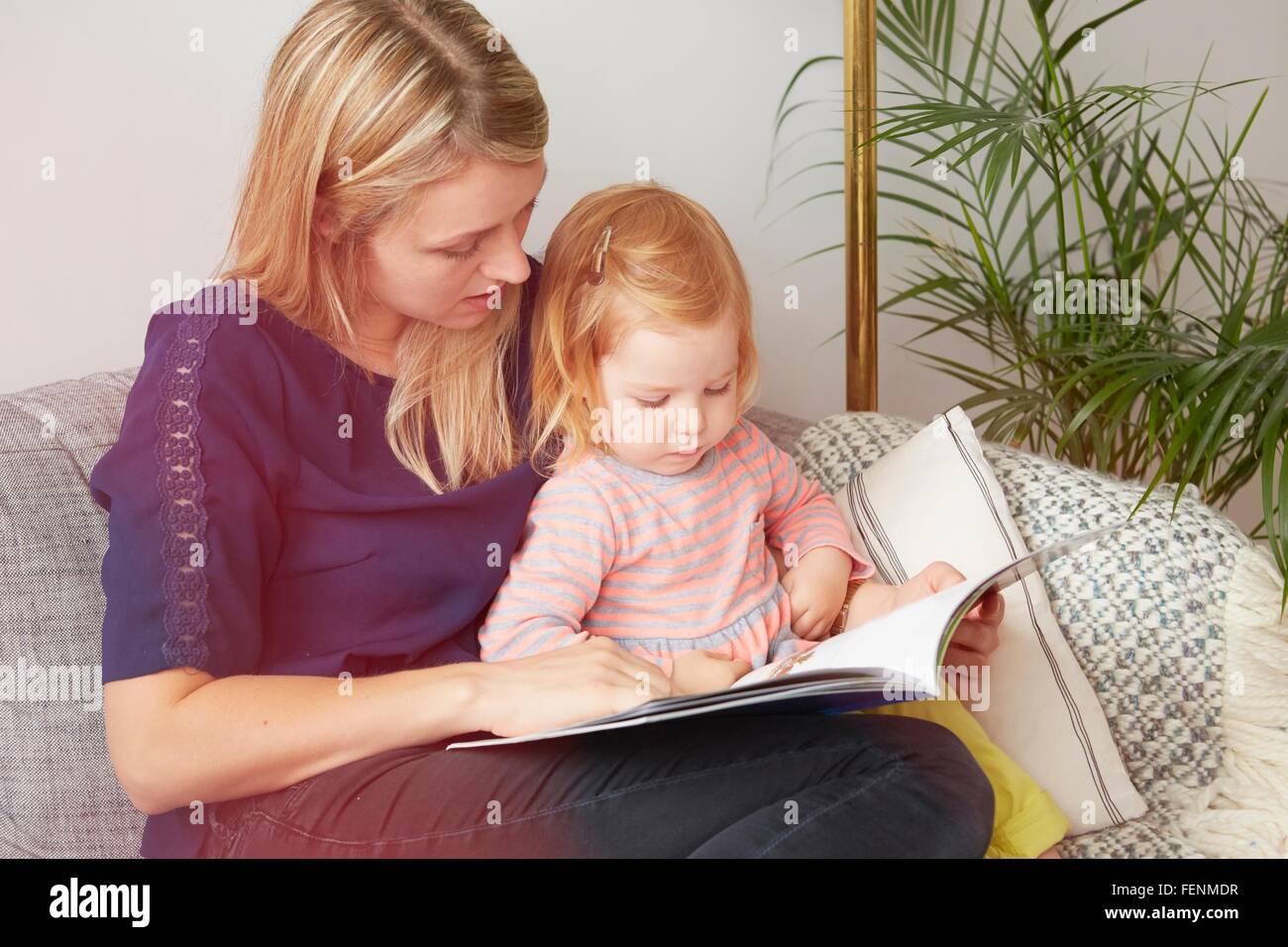 Frau und Kleinkind Tochter lesen auf dem Sofa im Wohnzimmer Stockfoto