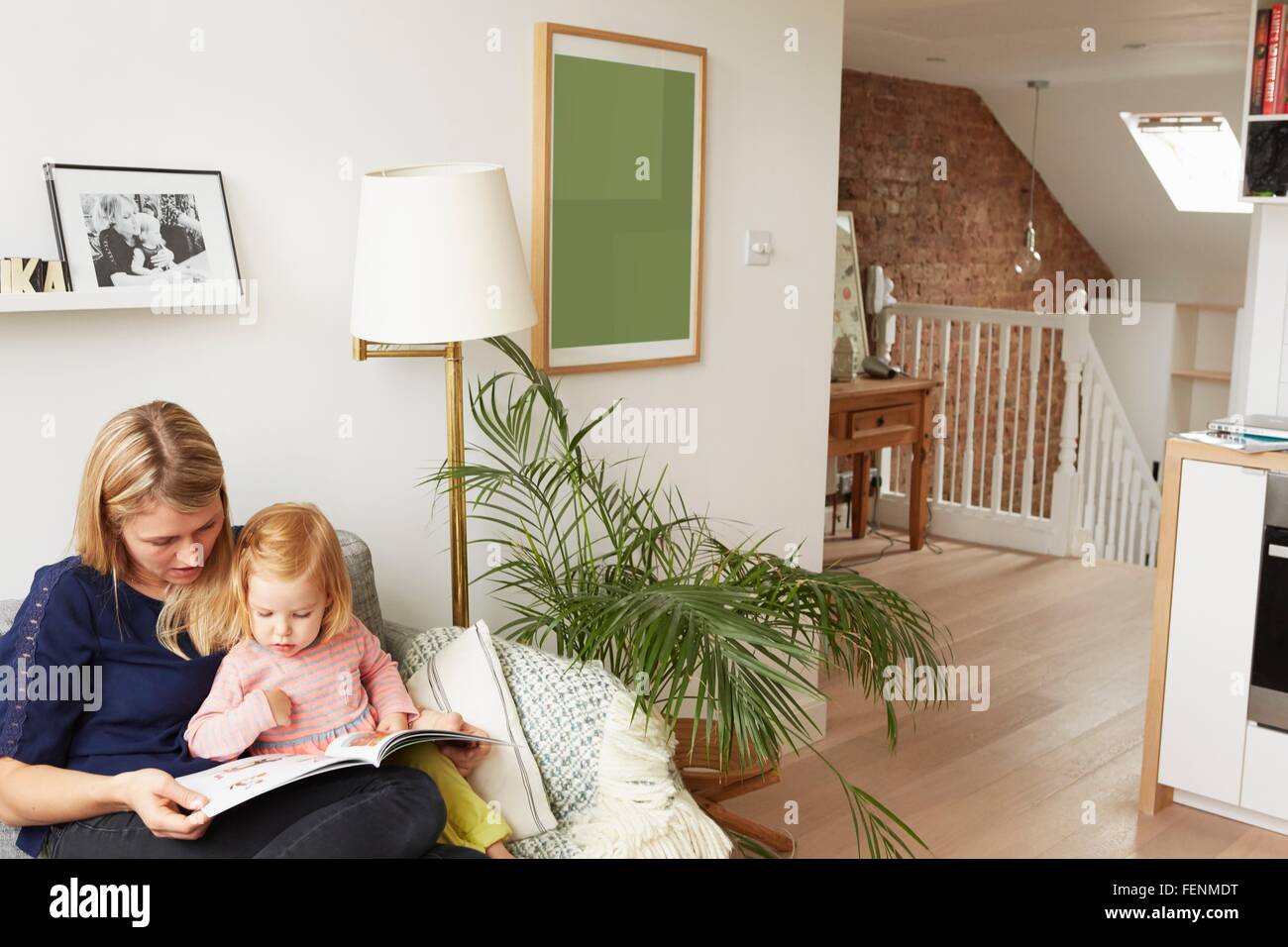 Frau und Kleinkind Tochter Lesebuch auf Sofa im Wohnzimmer Stockfoto