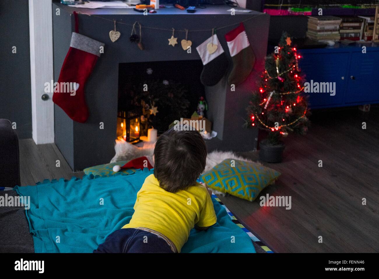 Rückansicht des männlichen Kleinkind liegend auf die Decke anzustarren Weihnachtsbaum vor Kamin Stockfoto