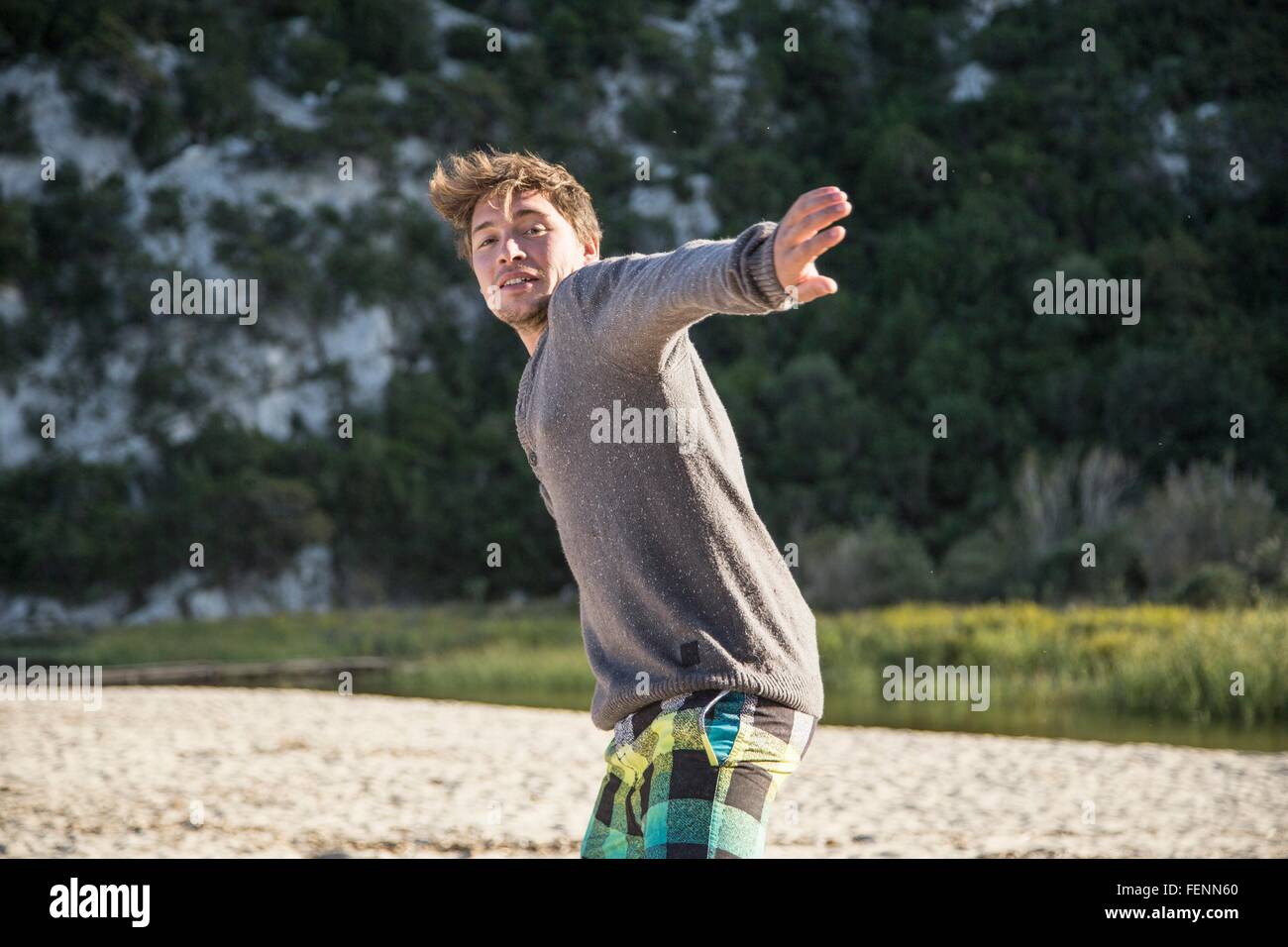 Vorderansicht des jungen Mannes am Strand bereit werfen Aktion, Blick in die Kamera Lächeln, Costa Smeralda, Sardinien, Italien Stockfoto
