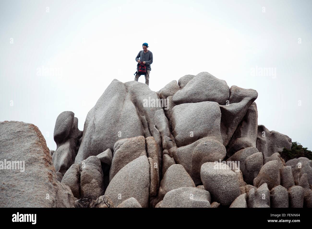 Niedrigen Winkel Ansicht der junge Mann auf Felsen mit Rucksack nach unten, Costa Smeralda, Sardinien, Italien Stockfoto