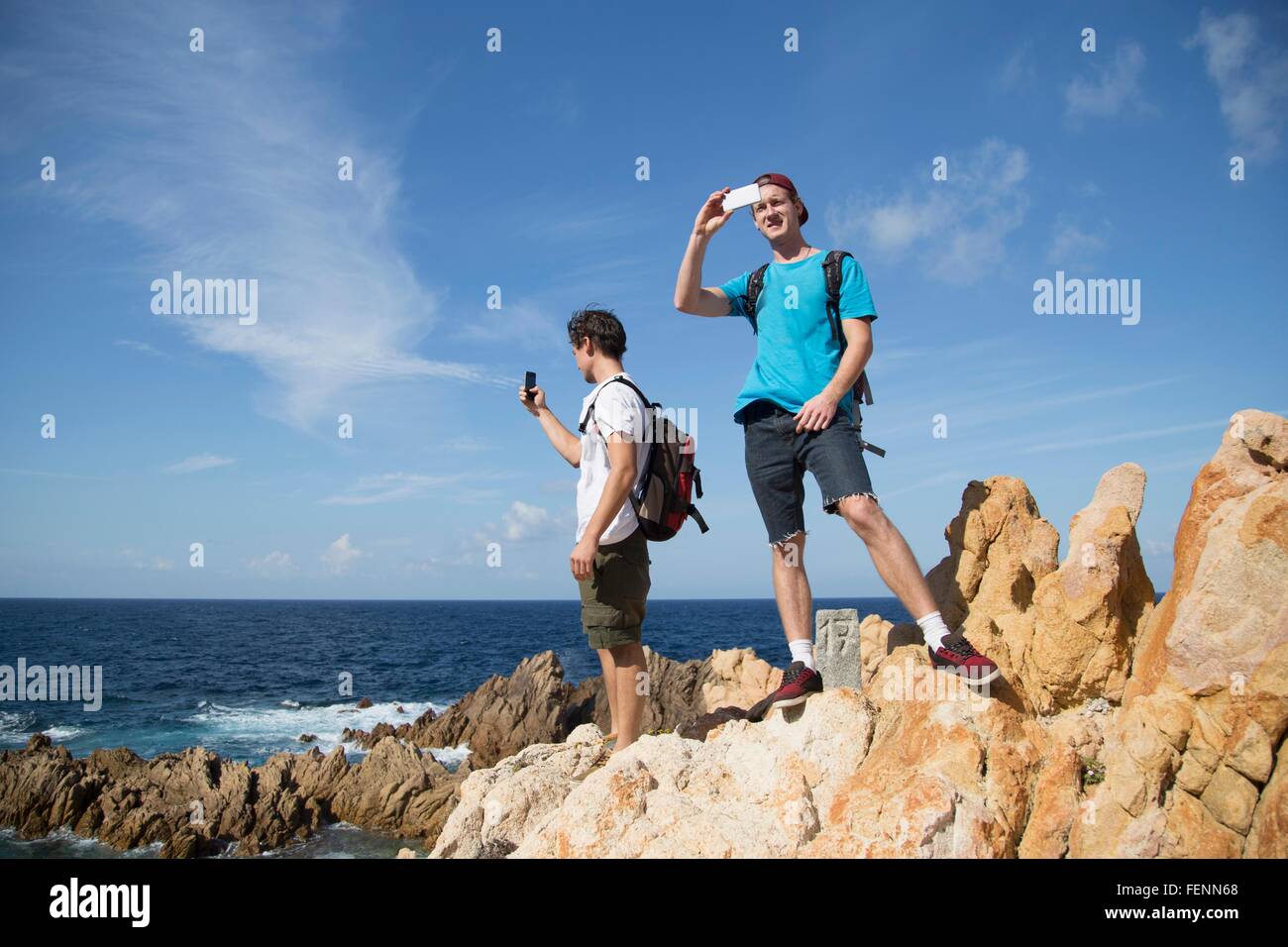 Junge Männer stehen auf Felsen mit Smartphone zu fotografieren, Costa Paradiso, Sardinien, Italien Stockfoto