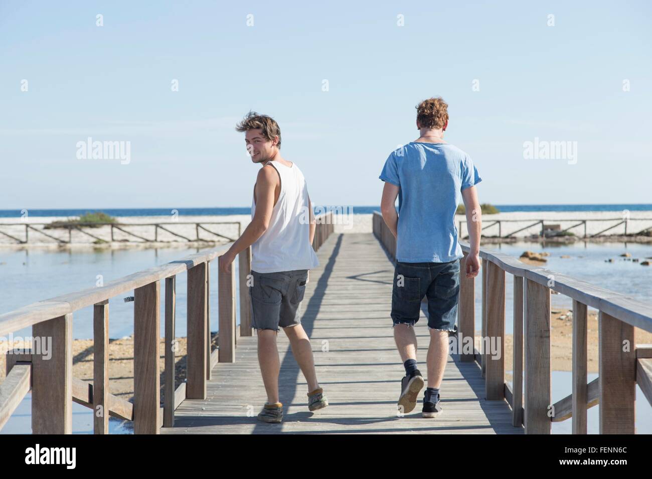 Voller Länge Rückansicht der jungen Männer zu Fuß auf hölzerne Pier über Schulter, Sardinien, Italien Stockfoto