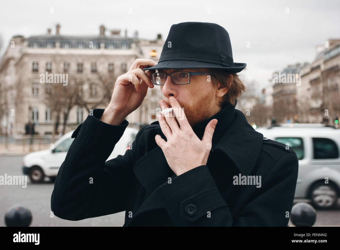 Attraktive bärtiger Mann mit Hut Rauchen auf der Straße in europäischen Stadt. Tiefenschärfe, Korn hinzugefügt. Stockfoto