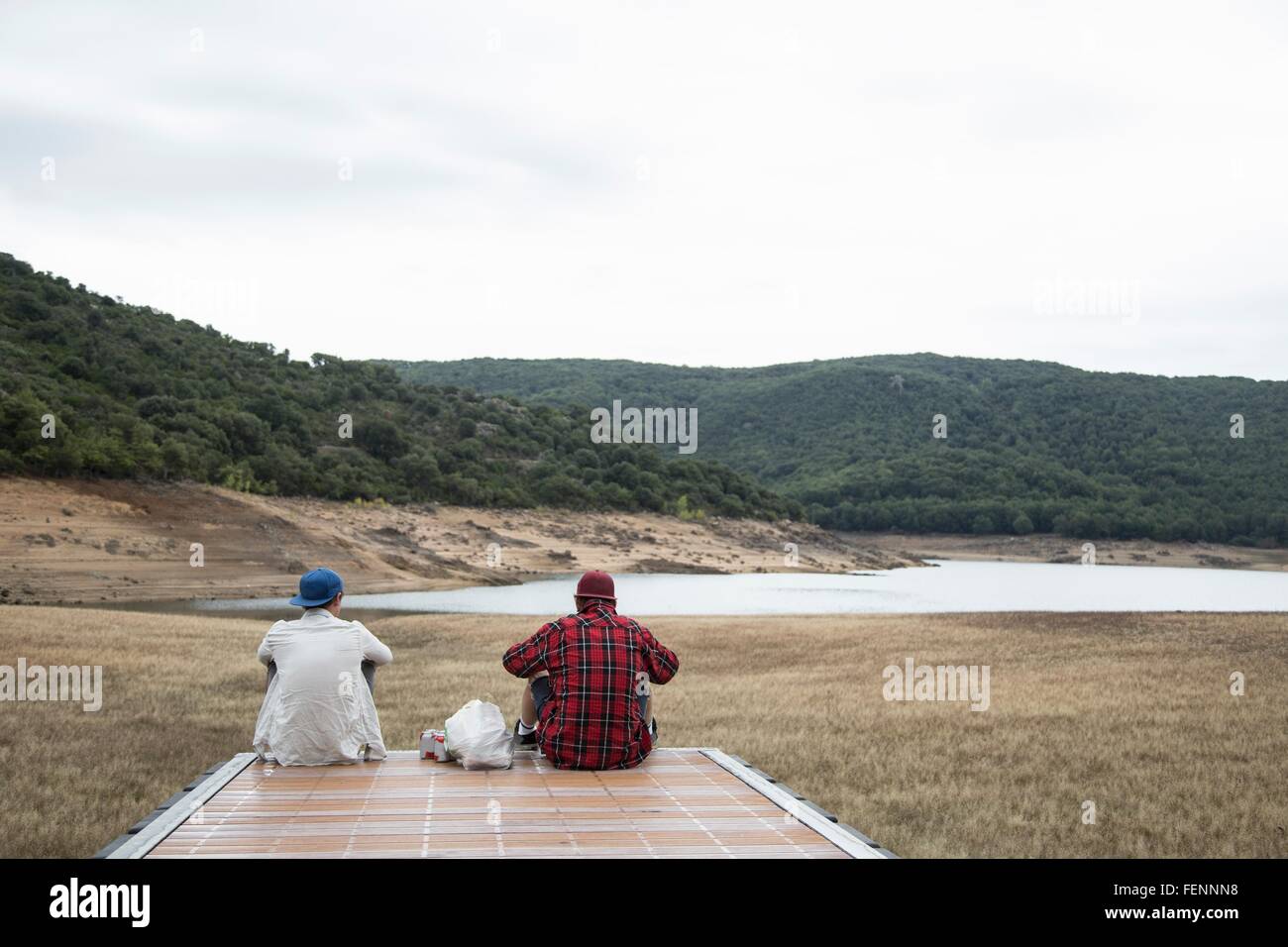 Rückansicht des junge Männer sitzen auf hölzerne Pier Blick auf Gebirge, Nuoro, Sardinien, Italien Stockfoto