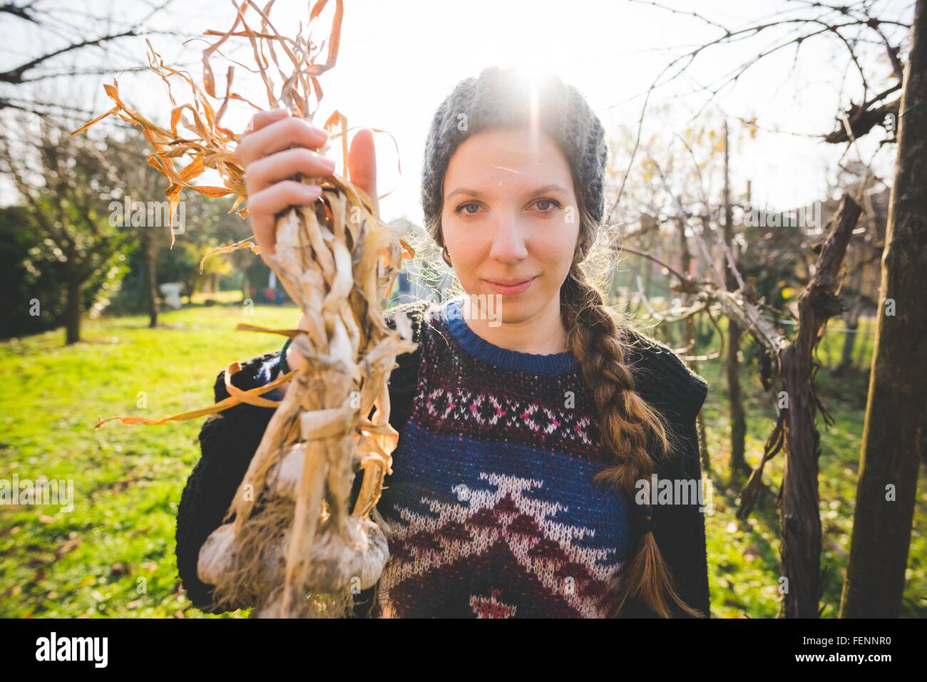 Junge Frau im Garten halten frisch gepflückt Knoblauch Zwiebeln, Blick auf die Kamera zu Lächeln Stockfoto