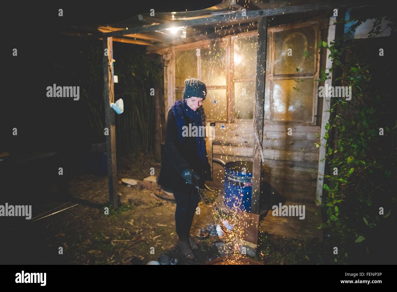 Junge Frau von Schuppen, die Zange über Feuer Funken verursacht, blickte lächelnd winkt Stockfoto