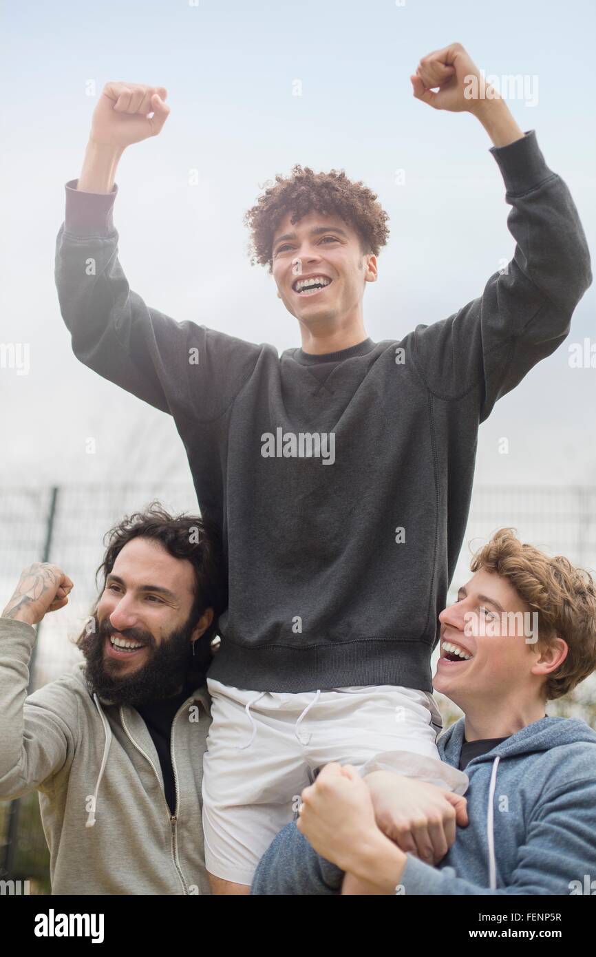 Junger Mann wird von zwei Freunden, feiern in Luft gehoben Stockfoto