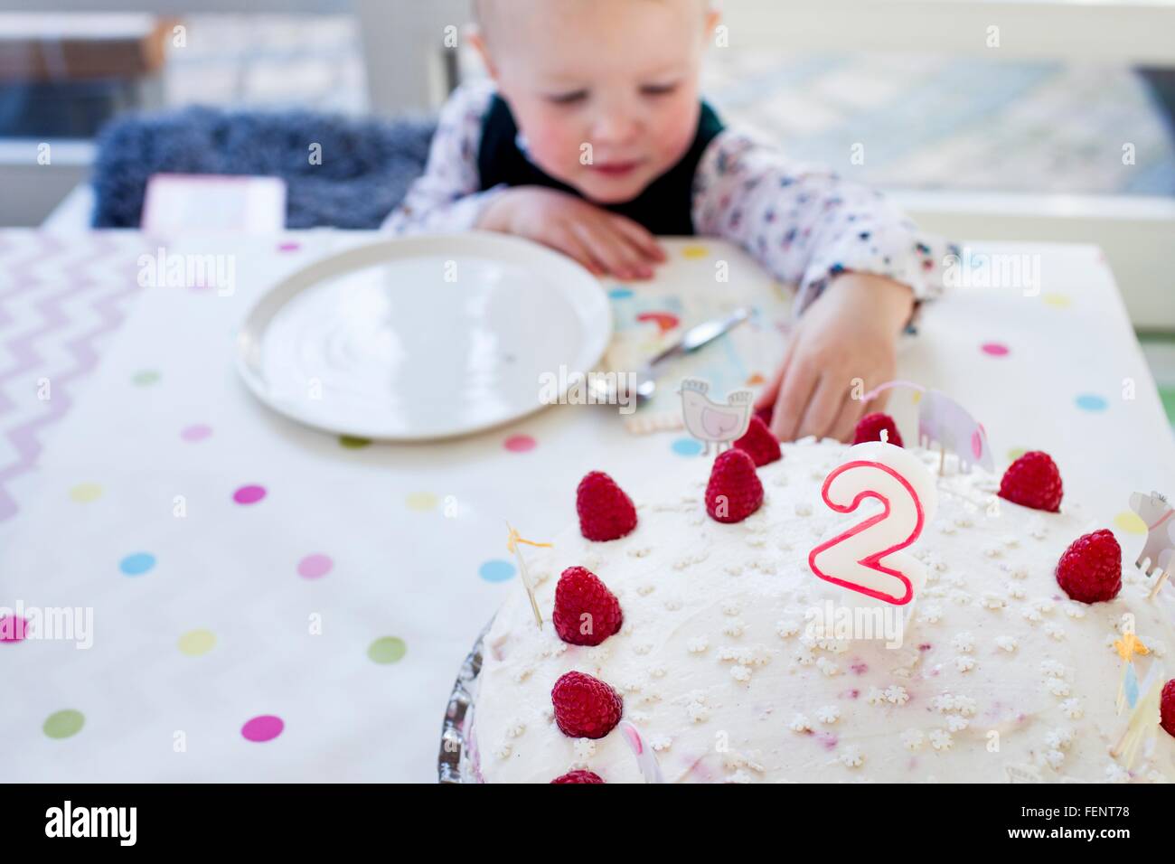 Weiblichen Kleinkind für Geburtstag Kuchen Himbeeren am Tisch zu erreichen Stockfoto