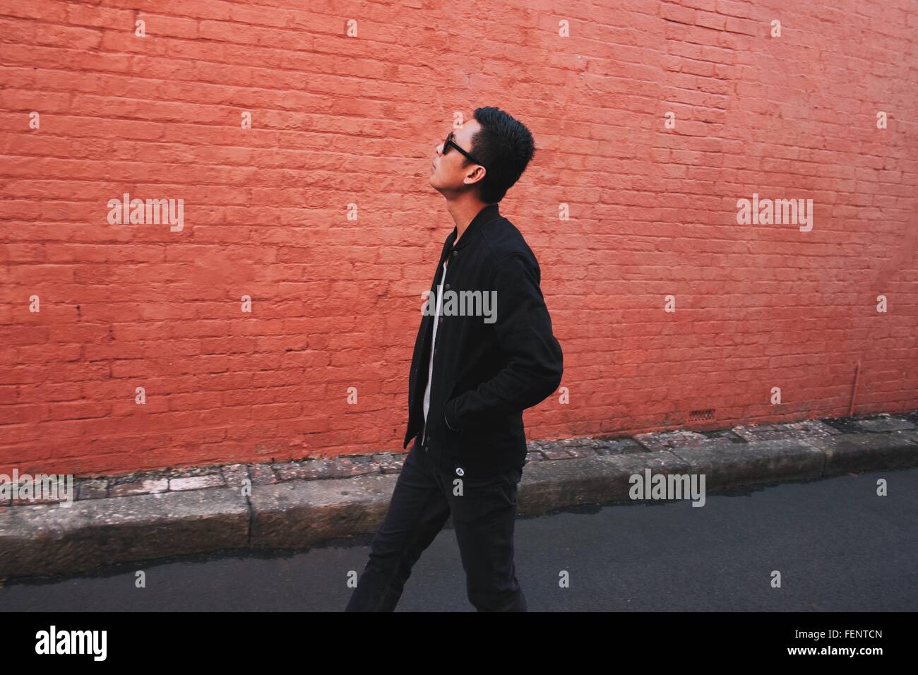 Seitenansicht des modischen jungen Mann gehen auf der Straße gegen roten Backsteinmauer Stockfoto