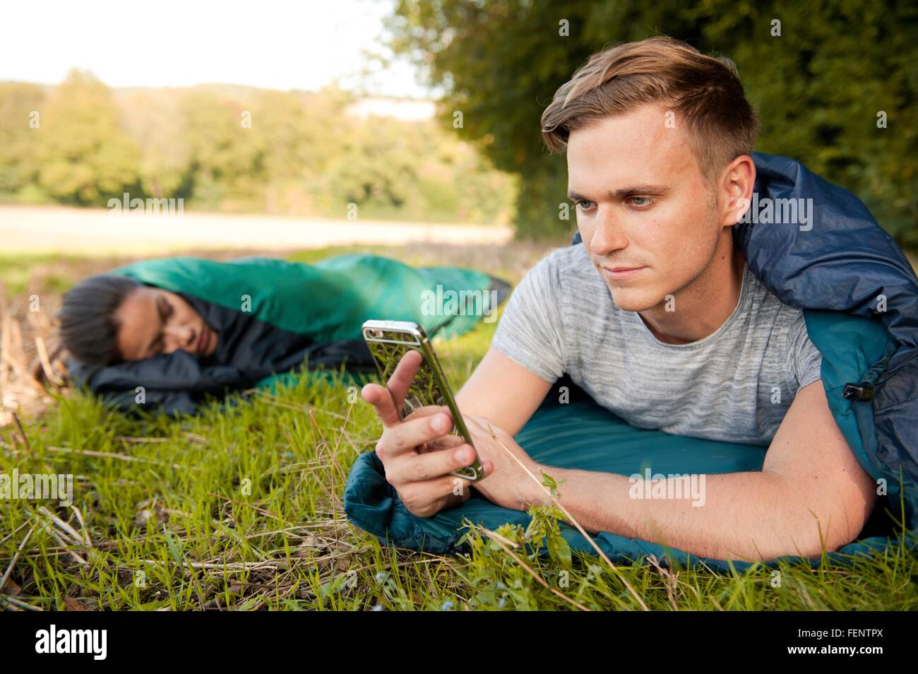 Junger Mann liegend Schlafsack SMS auf Smartphone im Feld Stockfoto