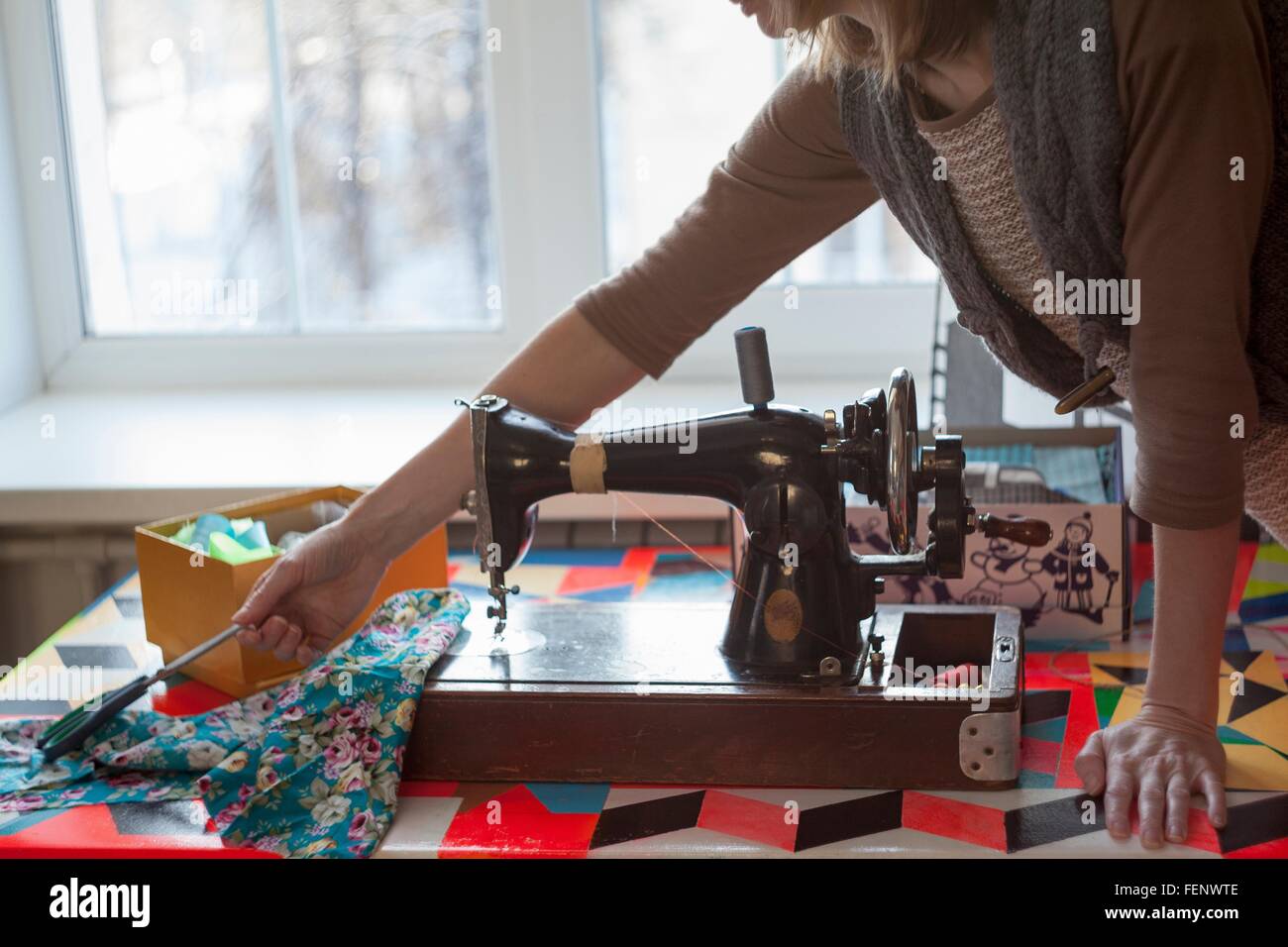 Frau mit Vintage Nähmaschine für Schere am Tisch zu erreichen Stockfoto