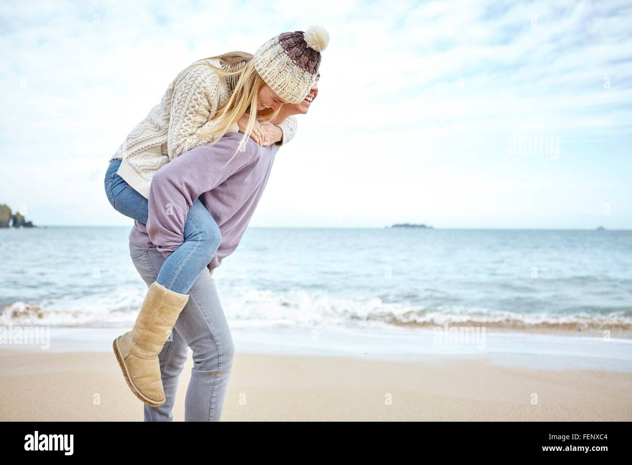 Junger Mann mit Freundin eine Huckepack auf Strand, Konstantin Bay, Cornwall, UK Stockfoto