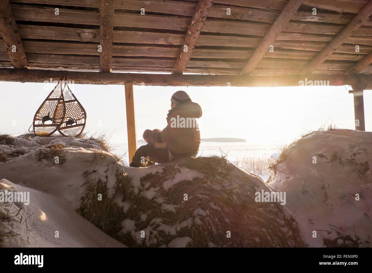 Mann sitzt auf verschneiten Heuhaufen in Scheune mit Schneeschuhen, Ural, Russland Stockfoto