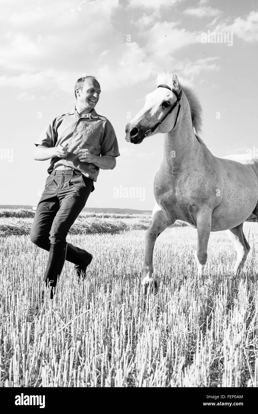 B&W Bild des männlichen Trainer läuft vor weißen Pferd im Feld Stockfoto