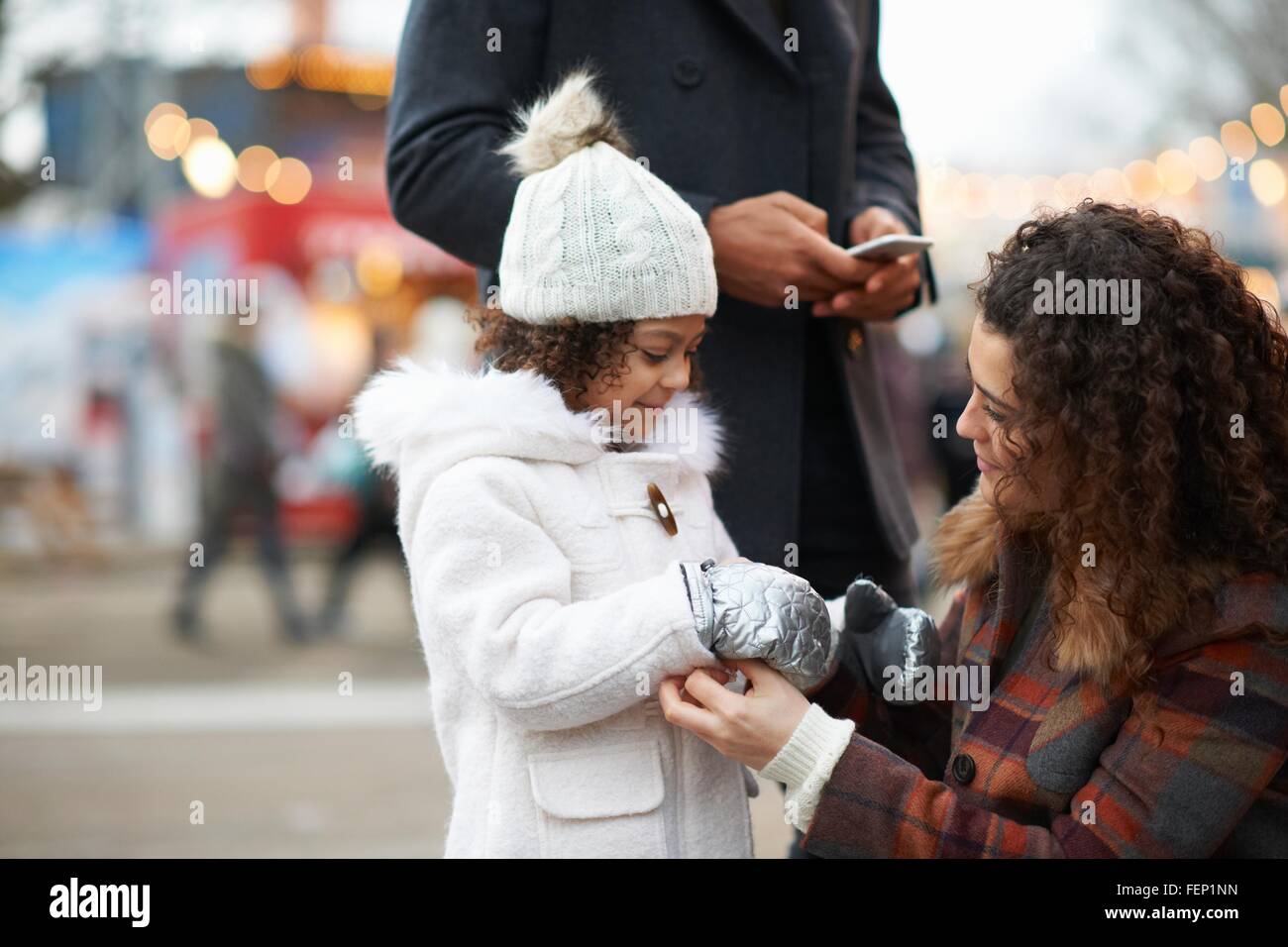 Hockender helfende Mutter Tochter Handschuhe anziehen Stockfoto