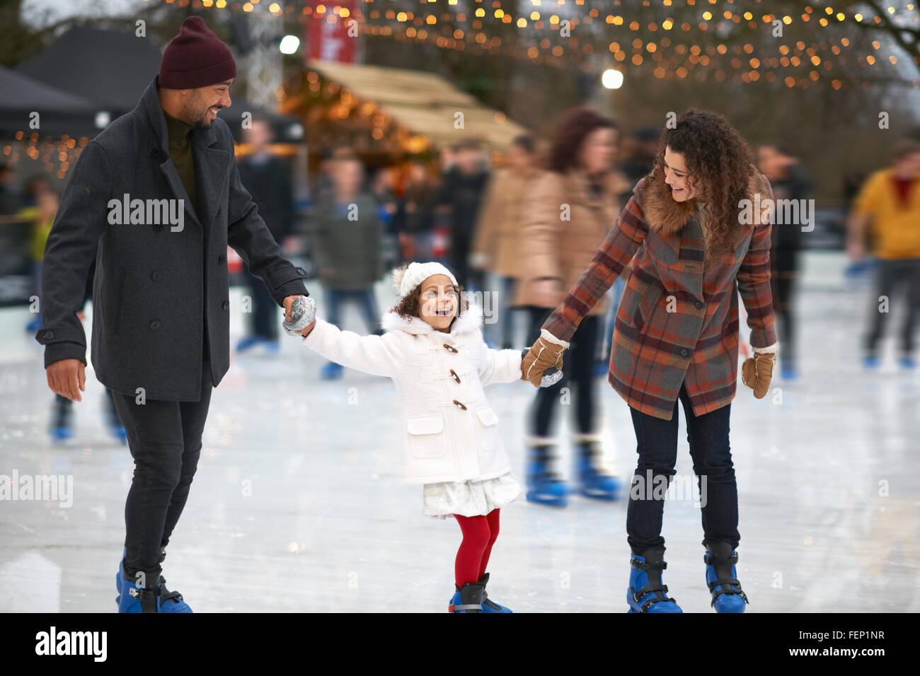 Mädchen halten Eltern Hände Eis Schlittschuhlaufen, Lächeln Stockfoto