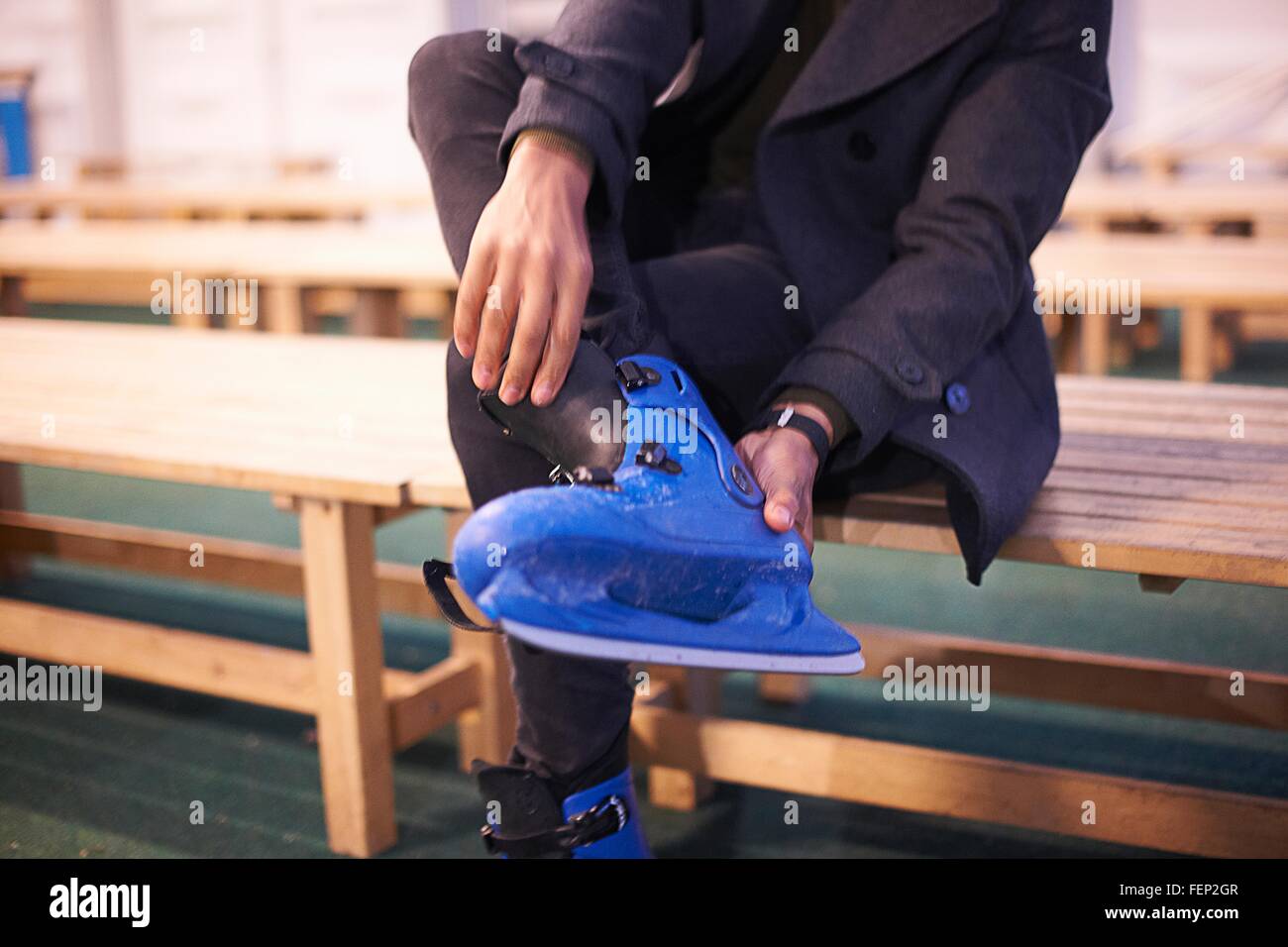 Brust nach unten Mitte erwachsener Mann sitzen auf Bank Schlittschuhe anziehen Stockfoto