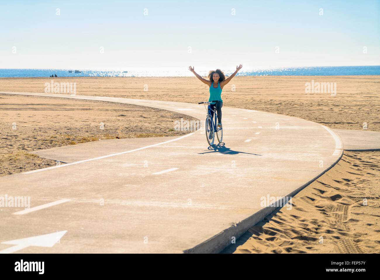Mitte Erwachsene Frau Radfahren entlang Weg am Strand, Arme in die Luft Stockfoto