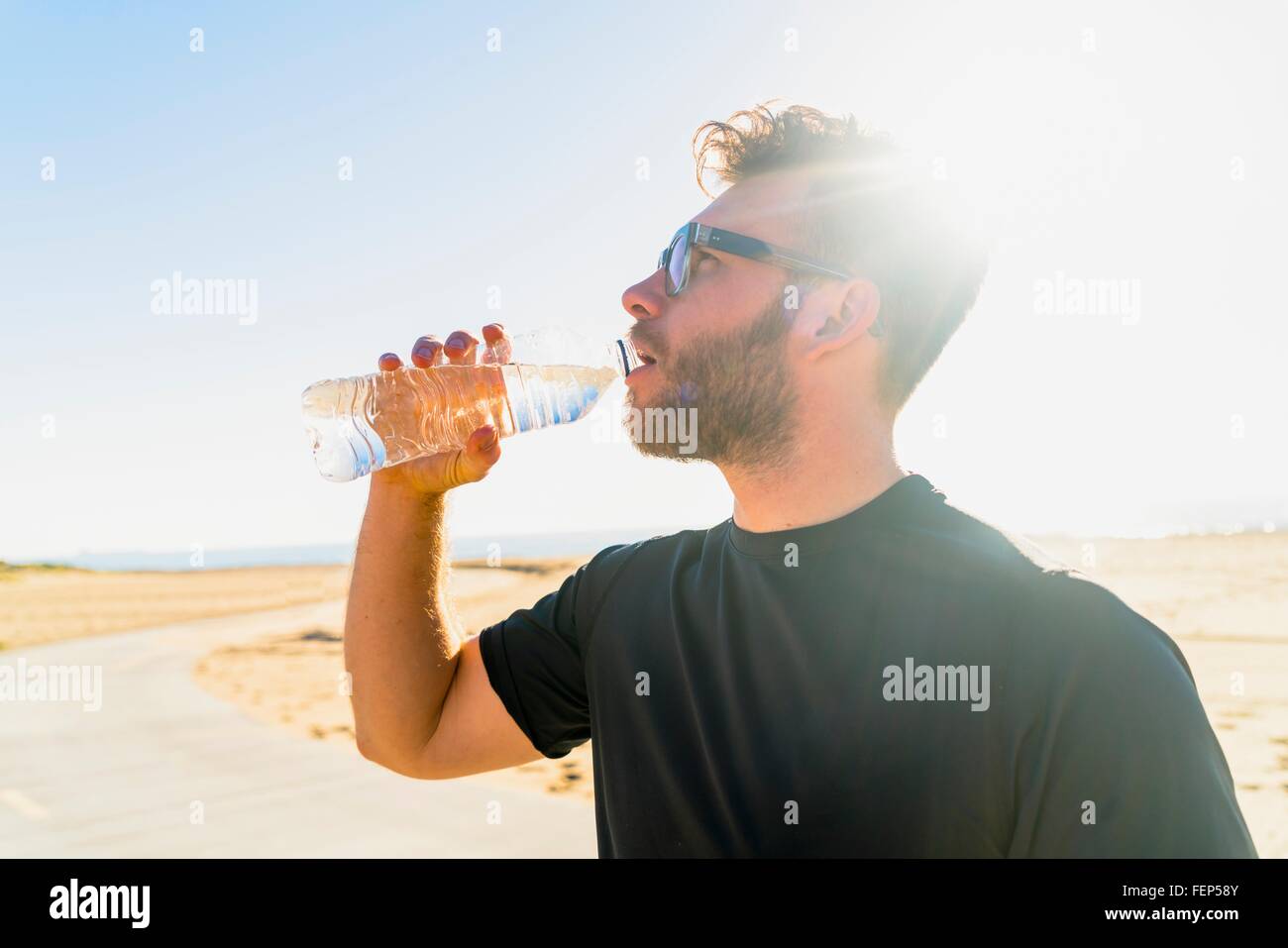 Junger Mann, Strand, trinken aus der Flasche Wasser Stockfoto
