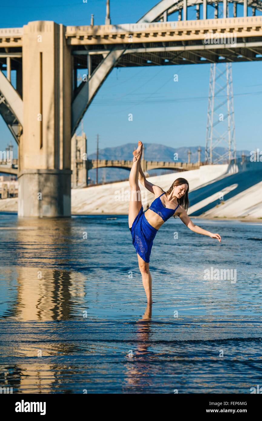 Tänzerin Knöchel tief im Wasser, Bein angehoben, balancieren auf einem Bein vor Brücke, Los Angeles, Kalifornien, USA Stockfoto