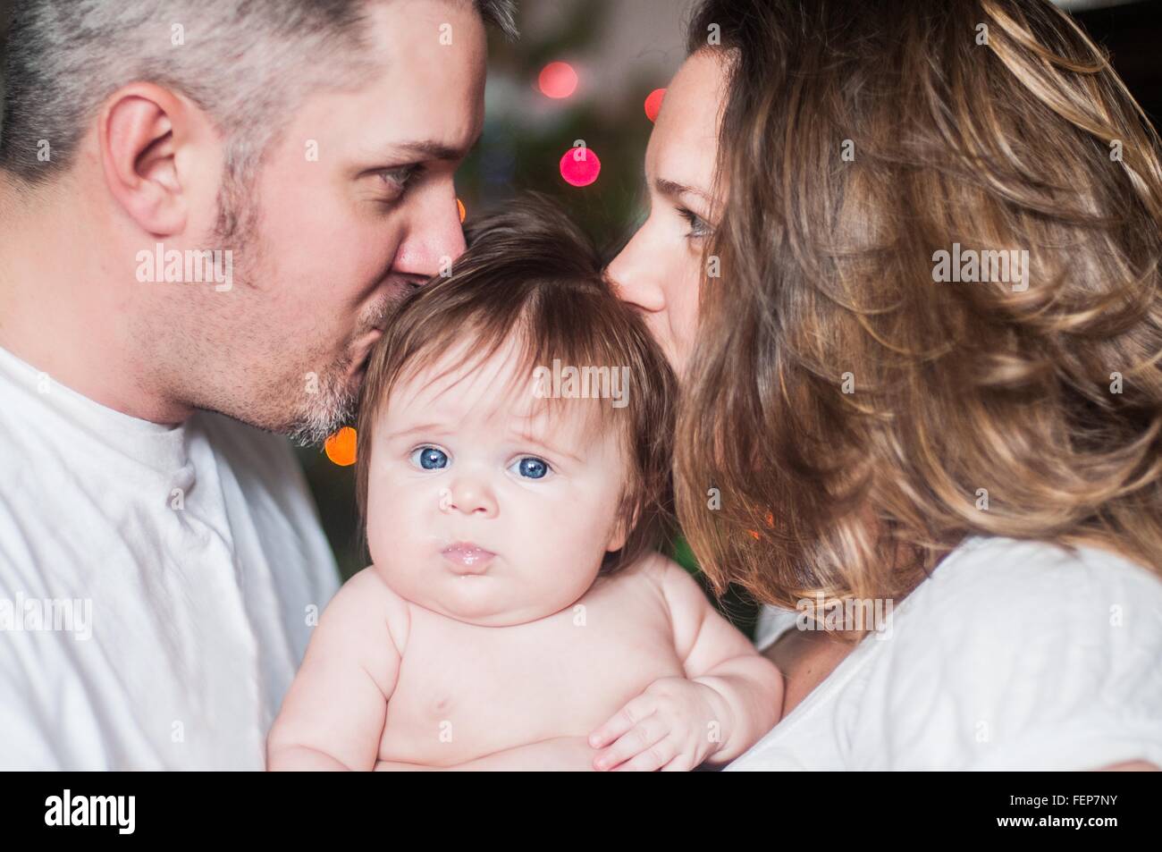 Mutter und Vater von Angesicht zu Angesicht halten Babymädchen, küssen auf Kopf Stockfoto