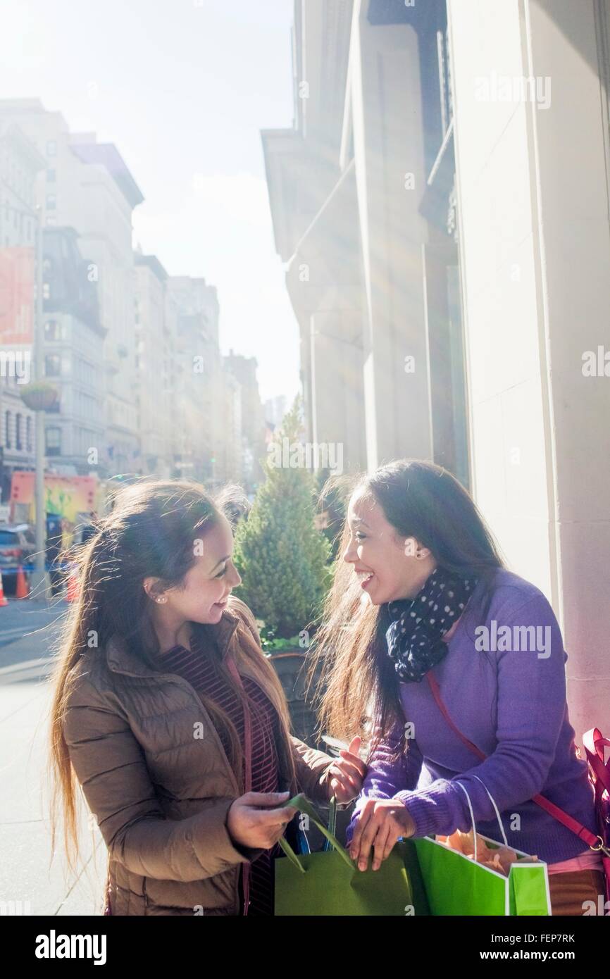 Junge weibliche Erwachsene Zwillinge mit Einkaufstüten, plaudern und Lachen auf Stadt Bürgersteig Stockfoto