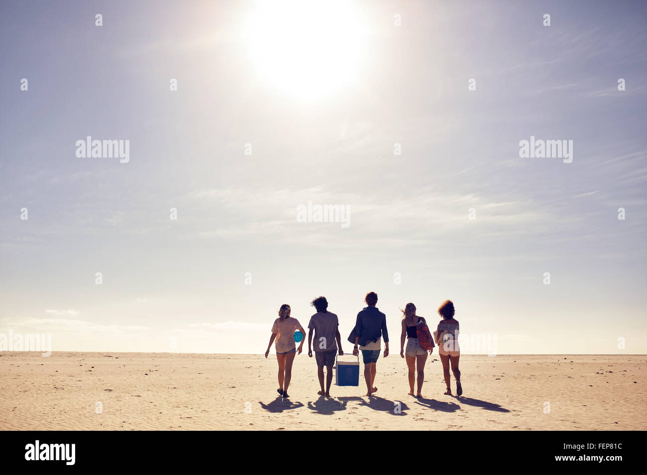 Hintere Ansicht Portrait junge Menschen, die die Kühlbox zu Fuß am Strand. Auf der Suche nach einem Ort für Party. Freunde am Strand vaca Stockfoto