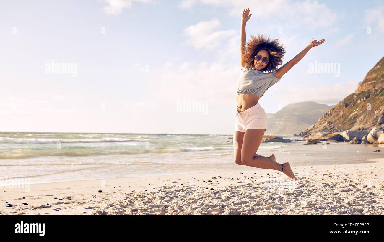 Porträt der schönen jungen Frau, die einen Sprung in der Luft am Strand. Afrikanische Frauen einen Sommertag am Meer zu genießen. Stockfoto