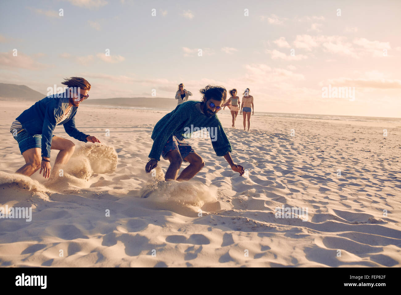 Junge Männer Rennen am Strand. Gruppe von Jugendlichen, die an einem Sommertag am Sandstrand spielen. Stockfoto