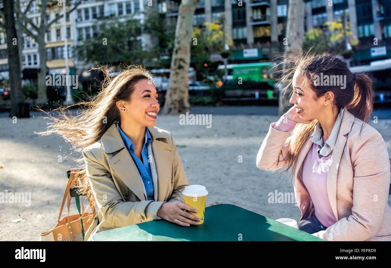 Junge Erwachsene weibliche Zwillinge reden und trinken Kaffee im Stadtpark Stockfoto