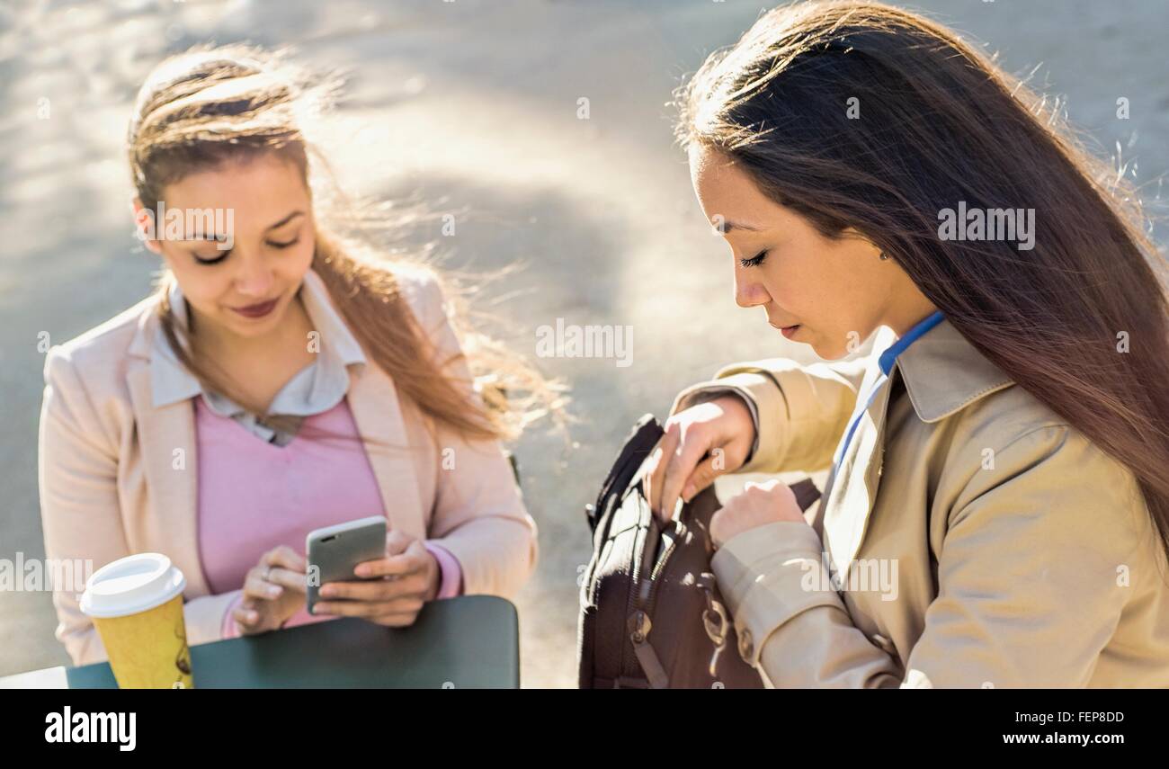 Junge Erwachsene weibliche Zwillinge lesen Smartphone Texte im Straßencafé Stockfoto