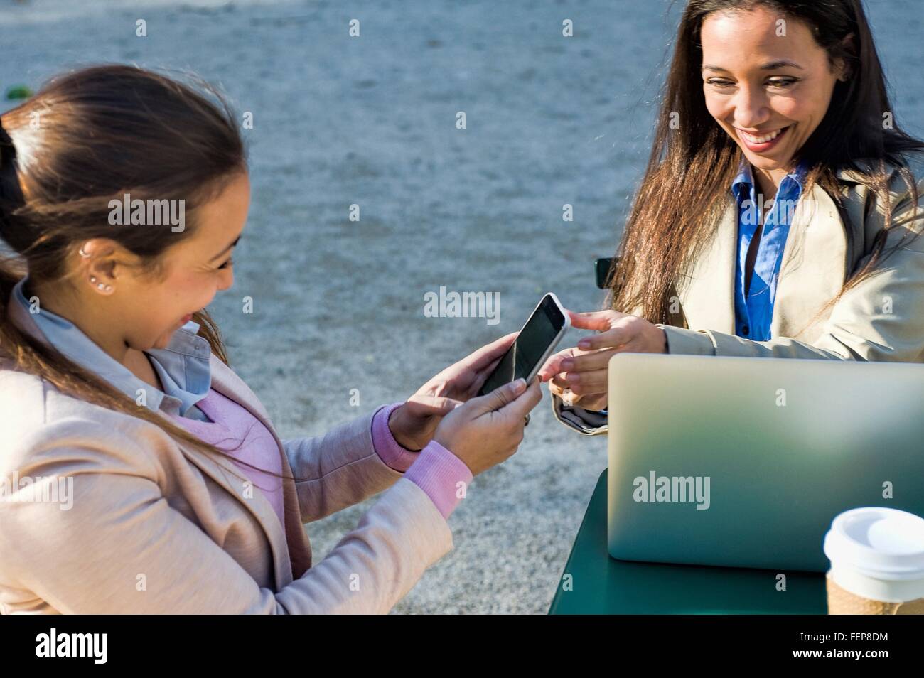 Junge Erwachsene weibliche Zwillinge mit Laptop und Smartphone im Straßencafé Stockfoto