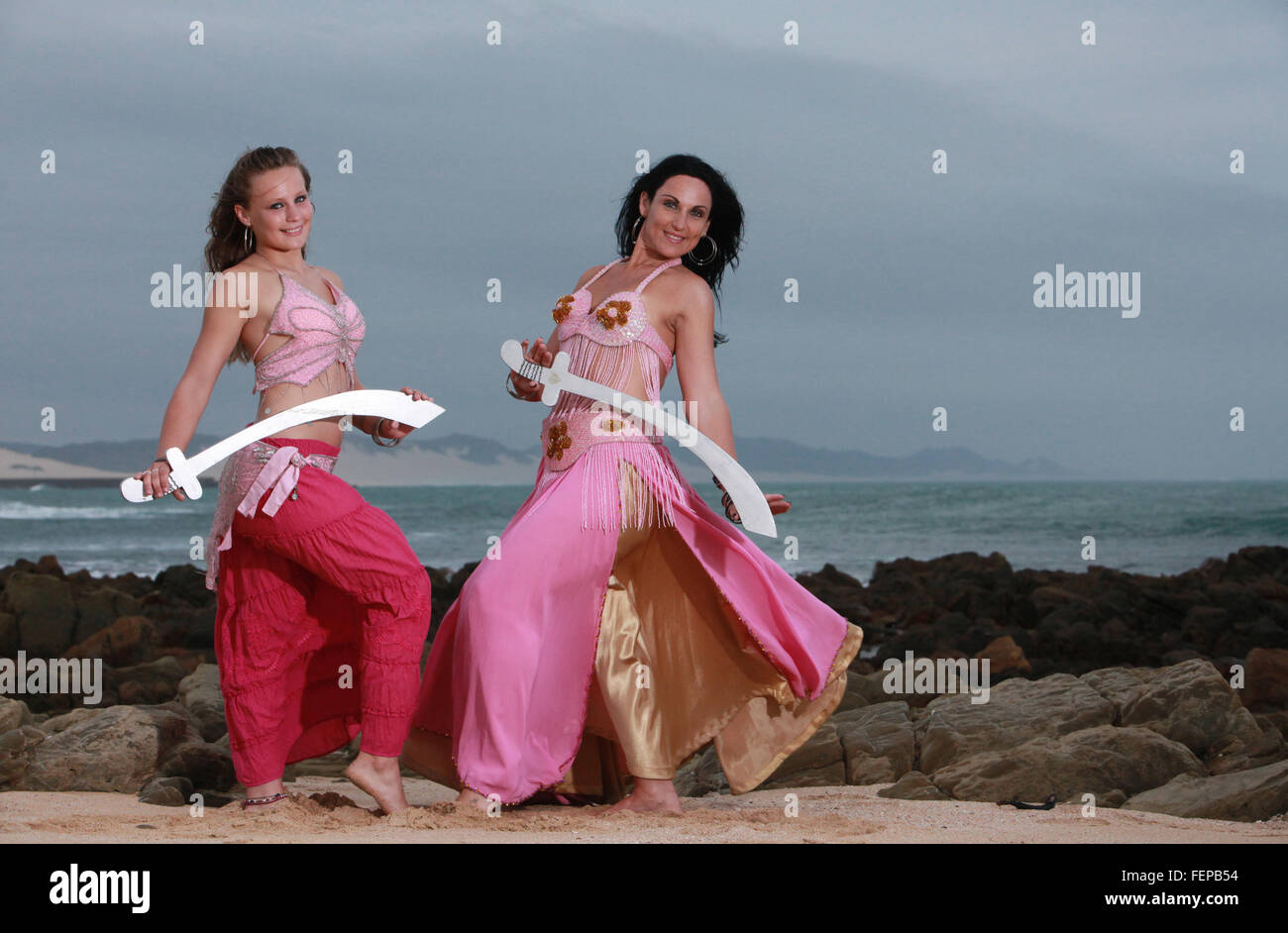 Eine Mutter und Tochter Kreuzung Schwerter oder kämpfen am Strand, sie sind beide Bauchtänzerinnen. Stockfoto