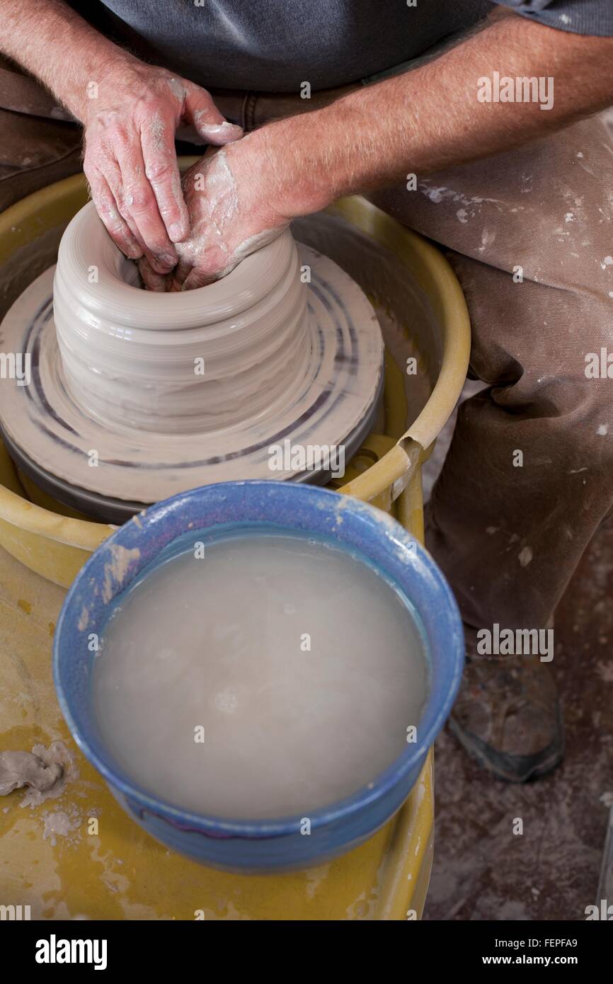 Beschnitten, erhöhte Ansicht der Töpfer Hände Gestaltung Tontopf auf der Töpferscheibe Stockfoto