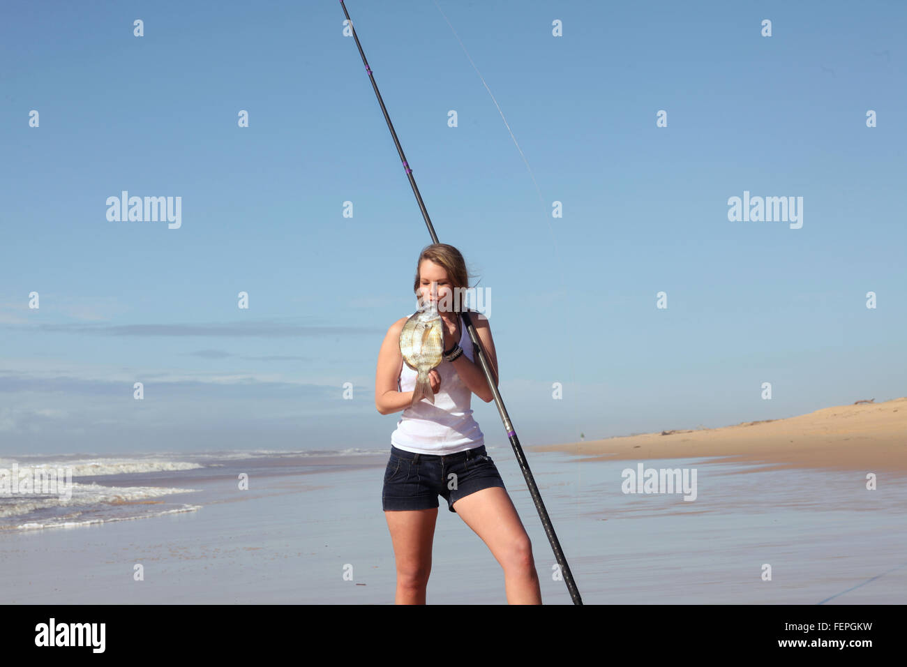 Eine schöne junge blonde Frau ist der Fisch, den, die Sie gerade gefangen, küssen, vor der Küste in Port Alfred, Südafrika. Sie hält Ihr Stockfoto