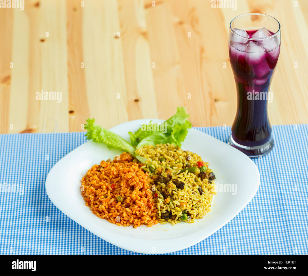 Leckere Gericht aus zwei Arten von Reis auf einem weißen Teller und ein Glas Saft mit Eis Stockfoto