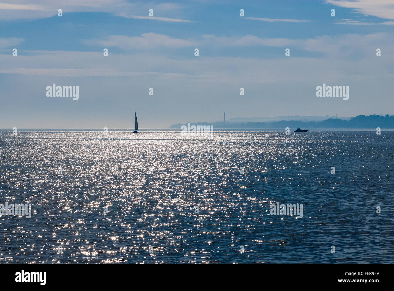 Segelboot und Motorboot auf Welligen spiegelnde Wasser gegen Ferne verschwommen Ufer und teilweise bewölktem Himmel. Stockfoto