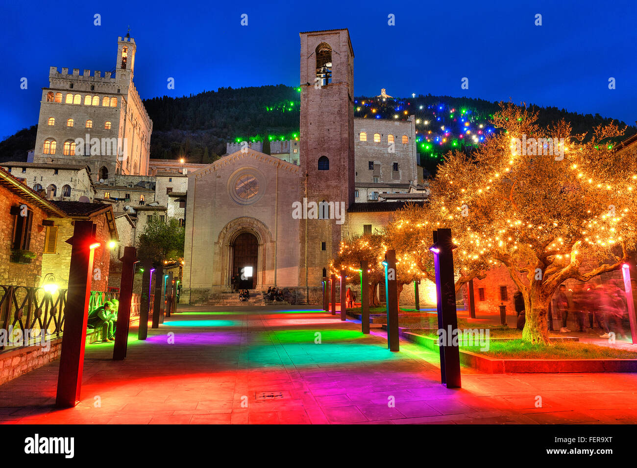 Gubbio, Umbrien, Italien in der Weihnachtszeit. Im Vordergrund die Kirche von San Giovanni zwischen Installationen von bunten Lichtern. Stockfoto