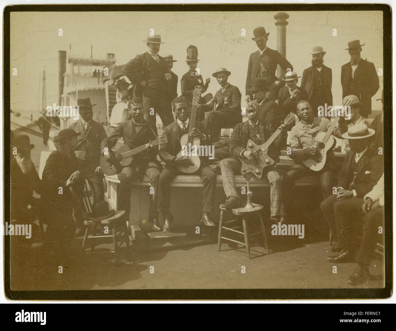 Eine afroamerikanische Minstrel-Gruppe wird auf einem Flussboot gezeigt, was die historische Bedeutung von Minstrel-Shows in der amerikanischen Unterhaltung, insbesondere im 19. Jahrhundert, widerspiegelt. Die Flussbooteinstellung ergänzt den historischen Kontext der Vorstellung. Stockfoto